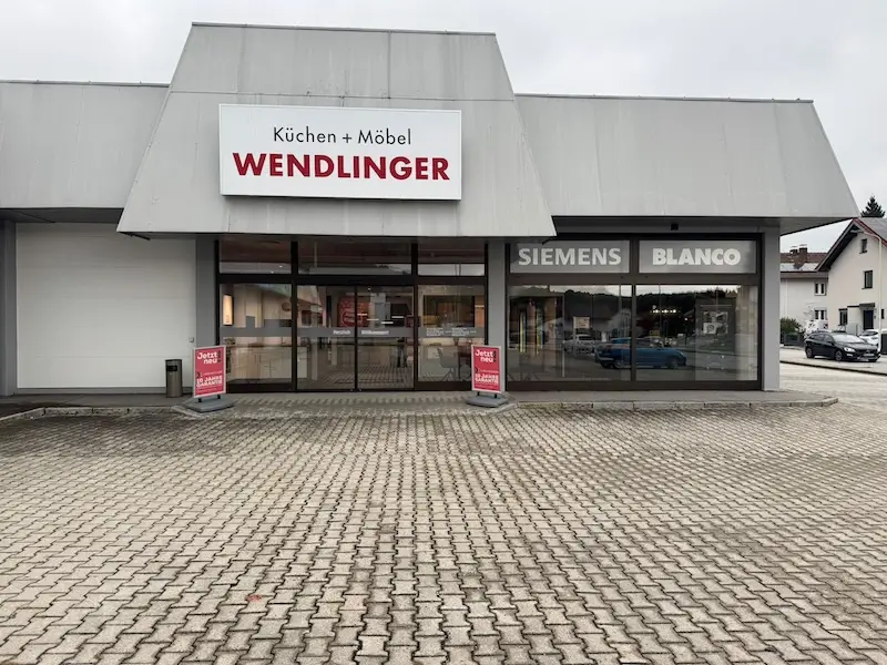 Fassade von Küchen + Möbel Wendlinger mit Schildern für Siemens und Blanco, leerer Parkplatz im Vordergrund.